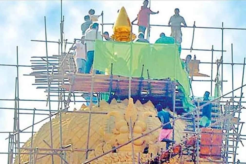Workers installing the golden kalasam atop a temple gopuram during Kumbabishekam renovation